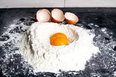 Granit mutfak tezgahında buğday unu ve yumurta sarısı yığını. Üst görünüm, yakın plan.