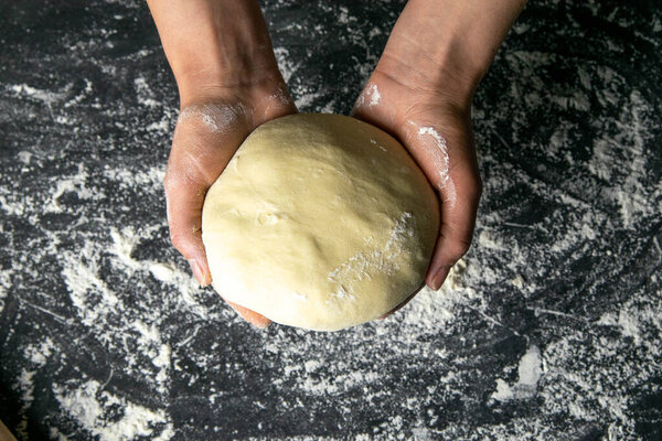 Strong woman's hands knead the dough on dark background. Top views, close-up.