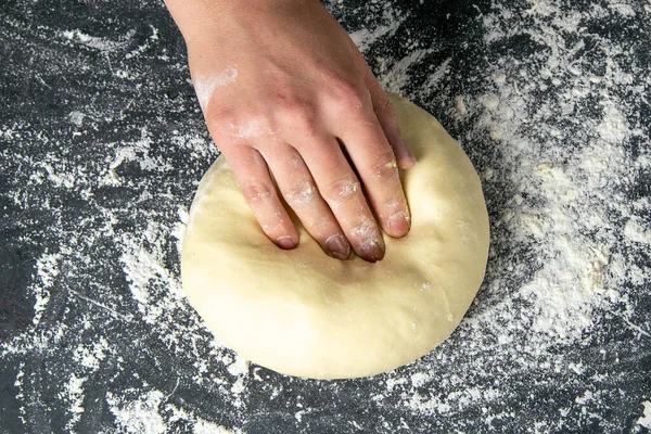 Strong woman\'s hands knead the dough on dark background. Top views, close-up.