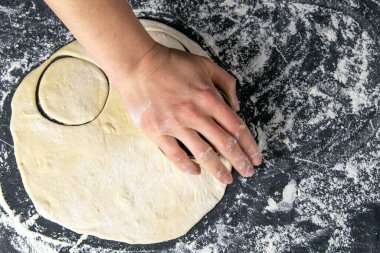 Koyu bir arka planda hamurdan çember kesme işlemi. Üst görünüm, yakın plan.