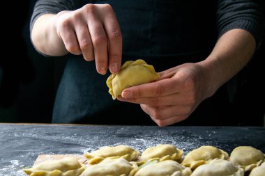 Koyu renk ceketli aşçı hamur tatlısı hazırlar. Bitmiş hamur köftelerinin serildiği karanlık bir masanın üzerinde. Ön manzara, yakın plan..