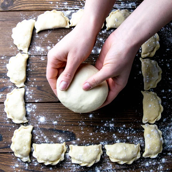 Strong woman\'s hands knead the dough on wooden background. Top views, close-up.