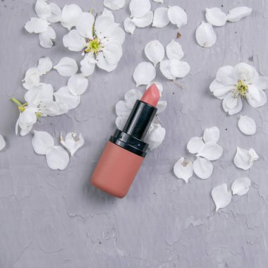 Gri makyaj masasında kozmetik seti. Üst görüş, yakın çekim. Ruj beyaz yapraklarla kaplı gri bir masada duruyor..