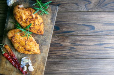 Baharatlı fırında tavuk göğsü, biberiye ahşap masada ahşap kesim tahtasında sarımsak. Açık alanlı en üstteki görünüm.