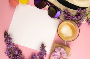 Etrafı leylak renkleri, güneş gözlükleri, renkli badem kurabiyeleri ve plaj şapkasıyla çevrili boş bir çarşaf. Şık, minimalist iş yeri konsepti. Kopyalama alanı olan üst görünüm.