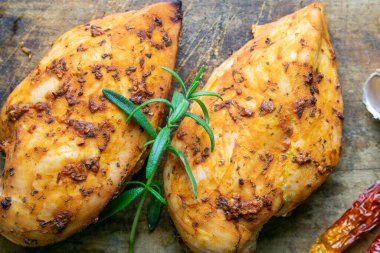 Baharatlı fırında tavuk göğsü, biberiye ahşap masada ahşap kesim tahtasında sarımsak. Üst görünüm, yakın plan.