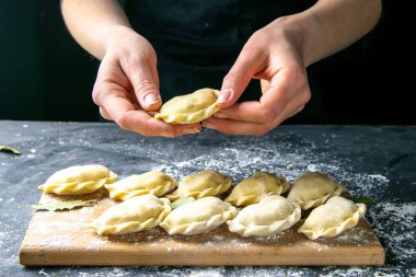 Koyu renk ceketli aşçı hamur tatlısı hazırlar. Bitmiş hamur köftelerinin serildiği karanlık bir masanın üzerinde. Ön manzara, yakın plan..
