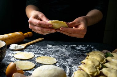 Koyu renk ceketli aşçı hamur tatlısı hazırlar. Bitmiş hamur köftelerinin serildiği karanlık bir masanın üzerinde. Ön manzara, yakın plan..