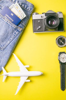 Retro kamera, pasaport, para, pusula, saat, oyuncak uçak ile seyahat konsepti. Sarı arka planda gezgin kıyafeti, turist gereksinimleri. Açık alanlı üst görünüm.