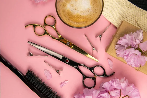 Hairdresser tools - scissors, combs and pink flowers with coffe on pink background. Beauty concept. Flat lay, top view.