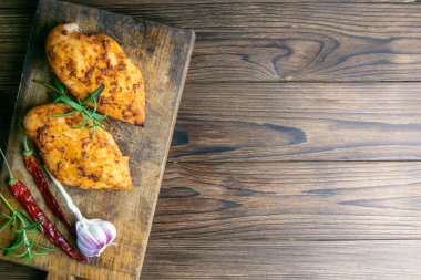 Baharatlı fırında tavuk göğsü, biberiye ahşap masada ahşap kesim tahtasında sarımsak. Açık alanlı en üstteki görünüm.