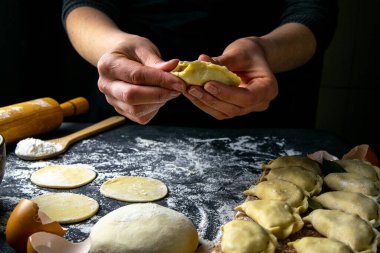 Koyu renk ceketli aşçı hamur tatlısı hazırlar. Bitmiş hamur köftelerinin serildiği karanlık bir masanın üzerinde. Ön manzara, yakın plan..