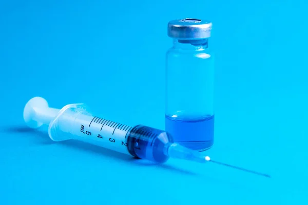 青い背景にコロナウイルスワクチンとガラスのバイアルと医療用注射器 — ストック写真