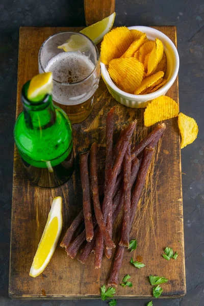 Fish caviar snack with beer, lemon and potato chips on dark wooden board. Snack on fish with beer. Close-up.