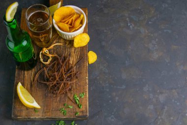 Koyu ahşap tahtada bira, limon ve patates cipsi ile mürekkep balığı ağı. Balığı birayla atıştır. Açık alanlı en üstteki görünüm.