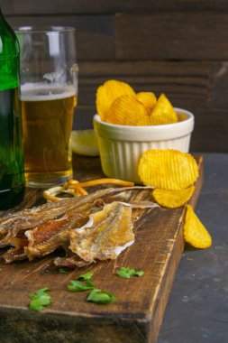 Gümüş Kehribar Balığı, biberli, limonlu ve patates cipsli koyu ahşap tahtada. Balığı birayla atıştır. Ön manzara, yakın plan..