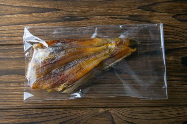 Şeffaf paket aperatifinde kurutulmuş mavi mezgit balığı ahşap arka planda bira için. Atıştırmalık balıktan biraya. Kapat..