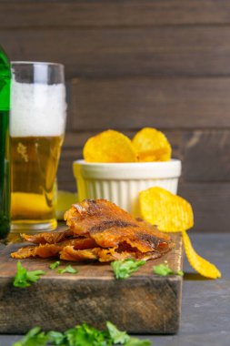 Koyu ahşap tahtada bira, limon ve patates cipsi ile kurutulmuş levrek. Balığı birayla atıştır. Ön manzara, yakın plan..