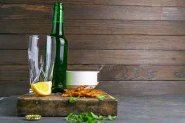 Koyu ahşap tahtada bira, limon ve patates cipsi ile kurutulmuş levrek. Balığı birayla atıştır. Açık alana sahip ön görünüm.