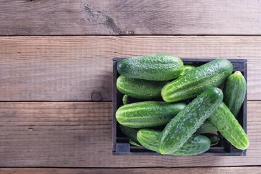 Eski ahşap masa manzaralı, taze salatalıklı bir kutu.