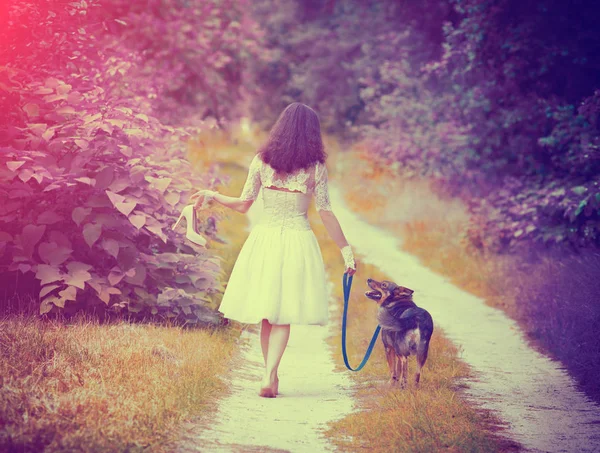 Young bride walking barefoot with dog on rural road — Stock Photo, Image