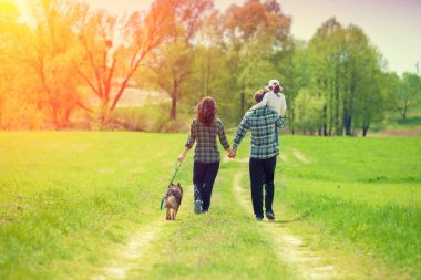 Kırsal toprak yolda yürüyen köpek ile mutlu bir aile. Babamın omzuna oturan küçük kız