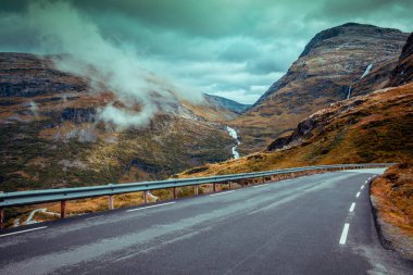 Bir araba sürüş dağ yolda. Yol dramatik fırtınalı bulutlu gökyüzü ile dağları arasında. Manzara. Güzel doğa Norveç.