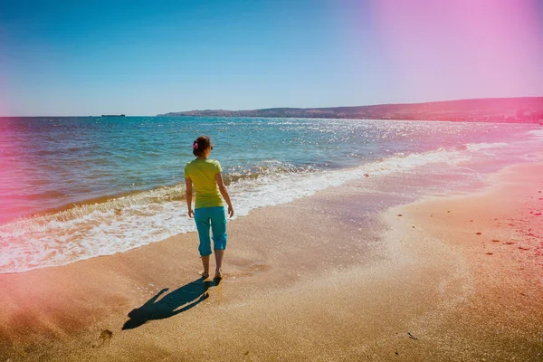 年轻快乐的女人赤脚走在沙滩上回到相机在日落 — 图库照片