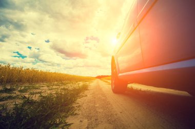 Güneşe doğru bir alanda kırsal toprak yol üzerinde bir araba sürüş