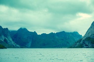 Kayalık sahil. Bulutlu gökyüzü ile özetlenen dağın tepesinde. Vahşi. Güzel doğa Norveç. Lofoten Adaları. Reine