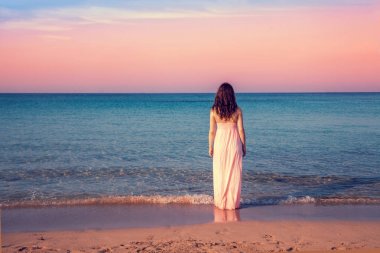 Sahilde günbatımı kameraya başa uzun elbiseli genç kadın