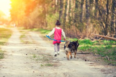 Yaz aylarında açık bir köpekle oynayan mutlu küçük kız. Köpek tasmasını tutan ve orman boyunca toprak yol üzerinde çalışan kız