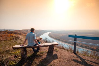 Vadide bir nehri olan dağ manzarası. Bir adam dağdaki bir bankta oturur ve gün batımında güzel bir manzaraya bakar.