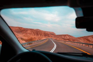 İsrail Dağı yolunda araba sürüyorum. Çöl manzarası. Boş yol. Dağ manzarası arabasından dramatik bir fırtınalı gün batımı gökyüzü. İsrail