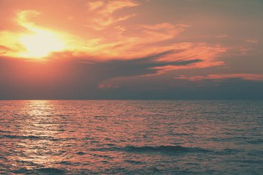 Akşamları turuncu bulutlu gökyüzü olan plaj. Denizin üzerinde gün batımı