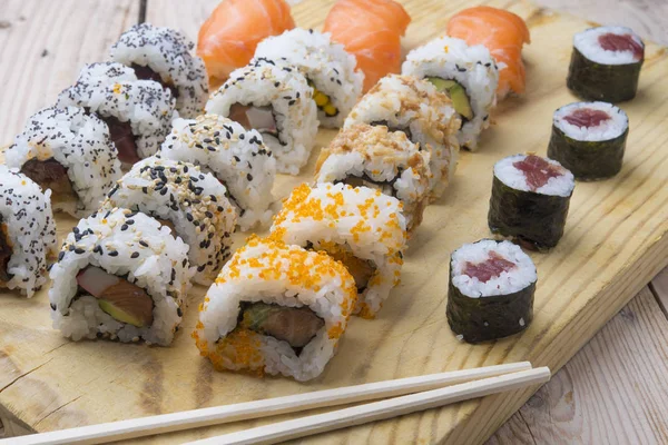 Diferentes rollos de sushi, wasabi y jengibre en un plato en bac de madera — Foto de Stock