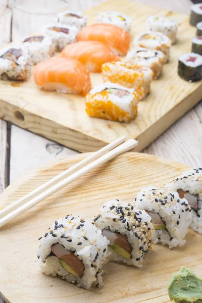 Diferentes rollos de sushi, wasabi y jengibre en un plato en bac de madera — Foto de Stock