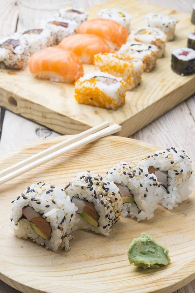 Diferentes rollos de sushi, wasabi y jengibre en un plato en bac de madera — Foto de Stock