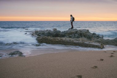 woman standing on coastal rocks on beach looking at the sea