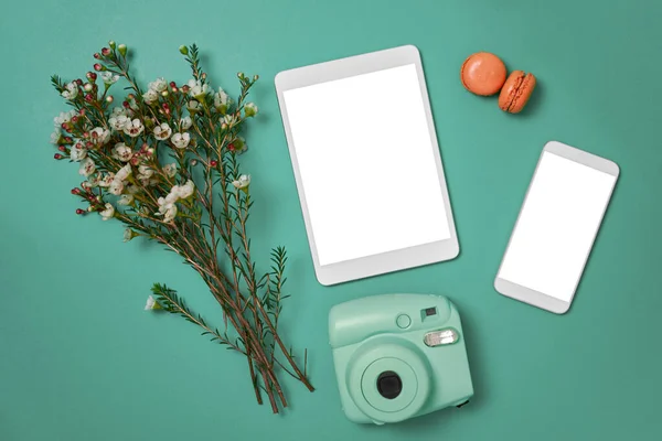 Piso con tablet, teléfono, cámara analógica, flores y macarrones rosados sobre fondo azul aguamarina — Foto de Stock