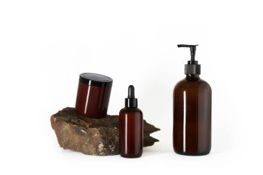 Koyu kahverengi şişeler kozmetik ürünler beyaz arka planda doğal taşlar izole edilmiş.