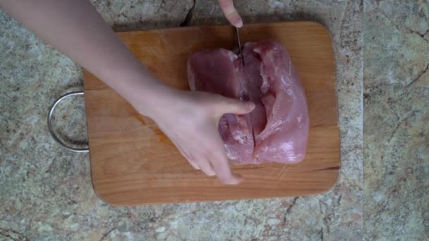 Mladá žena krájení krůty maso filet v plátcích s nožem na dřevěné desce na mramorovém stole — Stock video