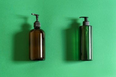Yeşil plastik kozmetik şişesi ve kahverengi cam şişe ve yeşil arka planda doğal ışık 