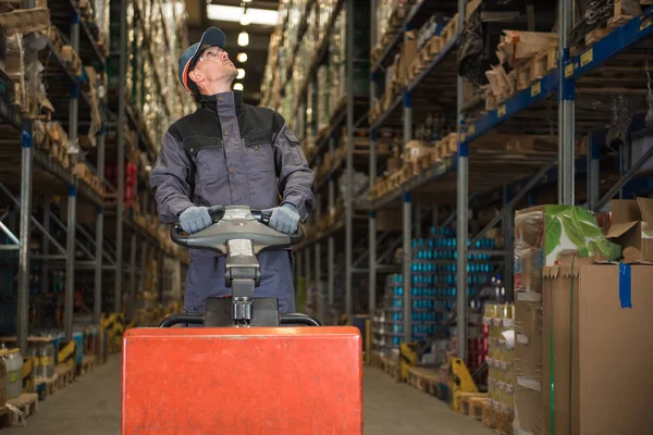 Trabalhador Caucasiano em uniforme com macaco palete à procura de pacote — Fotografia de Stock