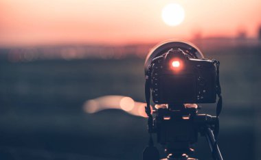 Günbatımı fotoğrafçılığı. Üç ayaklı kameranın renkli günbatımını çekmesi. Görüntü bulucudan geçen ışık.