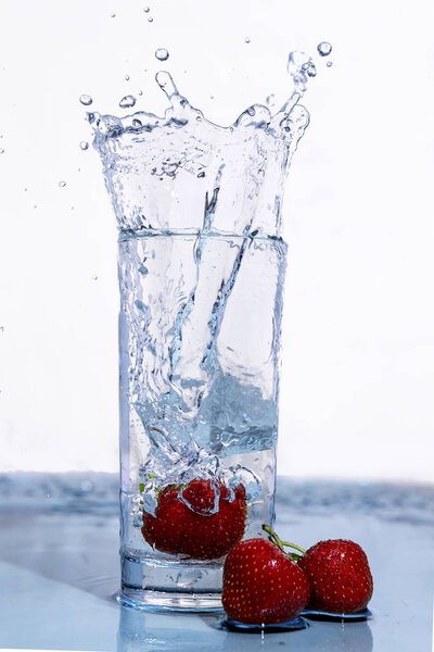 Strawberries fall into a glass of water.