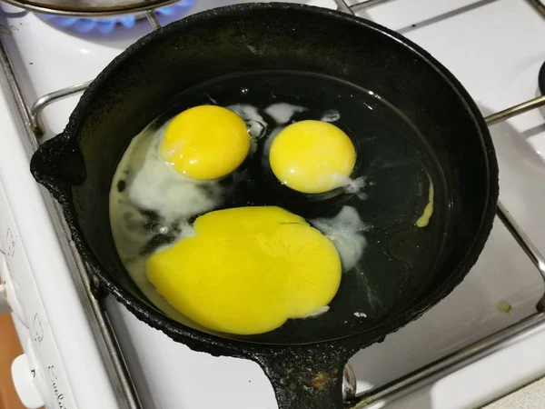 cooking fried eggs from 3 eggs in a black pan