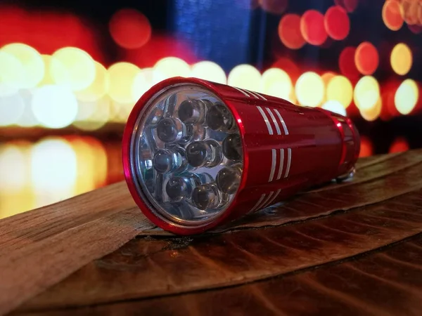 Red LED eco-friendly flashlight, against the background of the night lights of the city. Night illumination of cities.