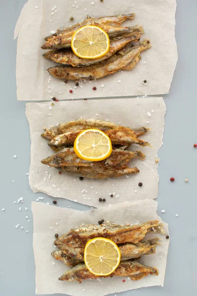 Capelin fritto con limone su carta da forno su sfondo grigio — Foto Stock