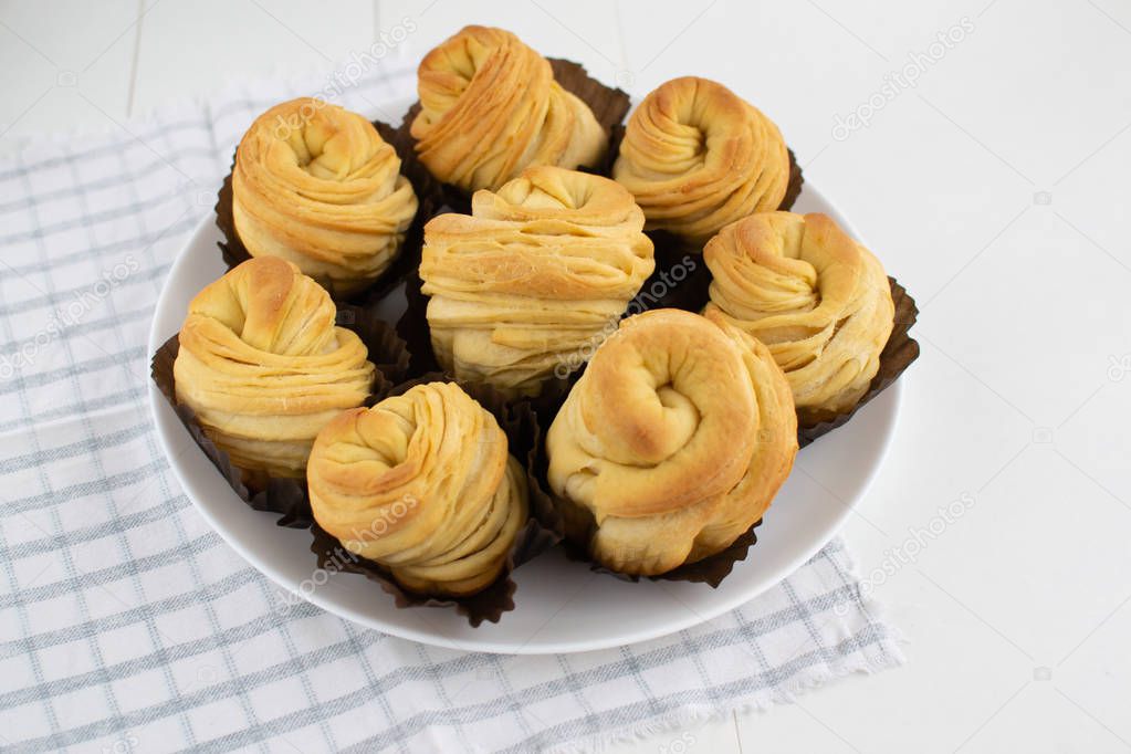 A lot of cruffins in brown paper forms on a white background